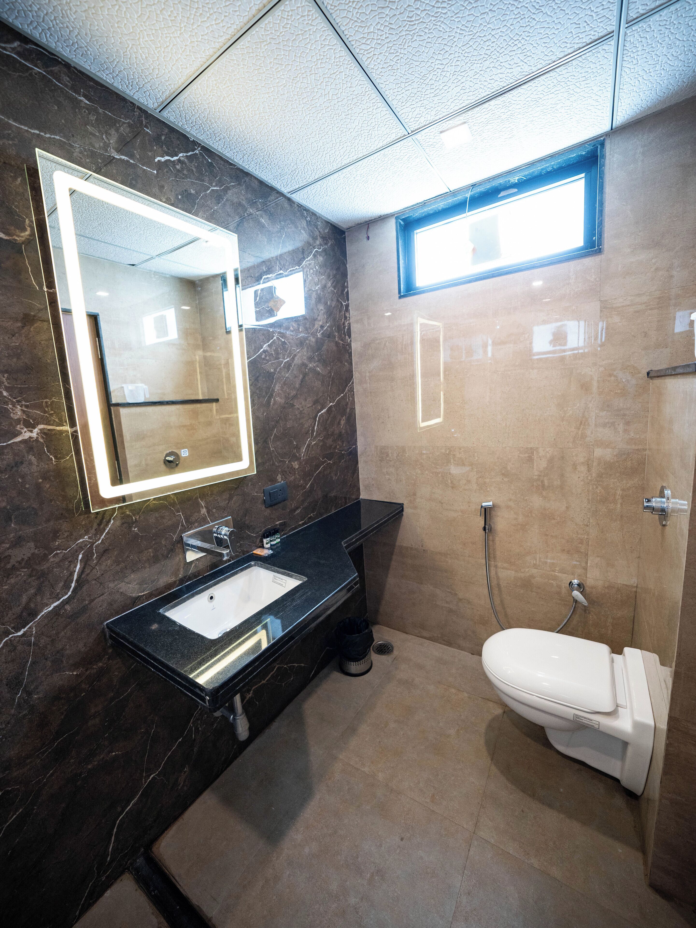 A modern bathroom with a marble vanity, a large mirror, a toilet, and a shower area.