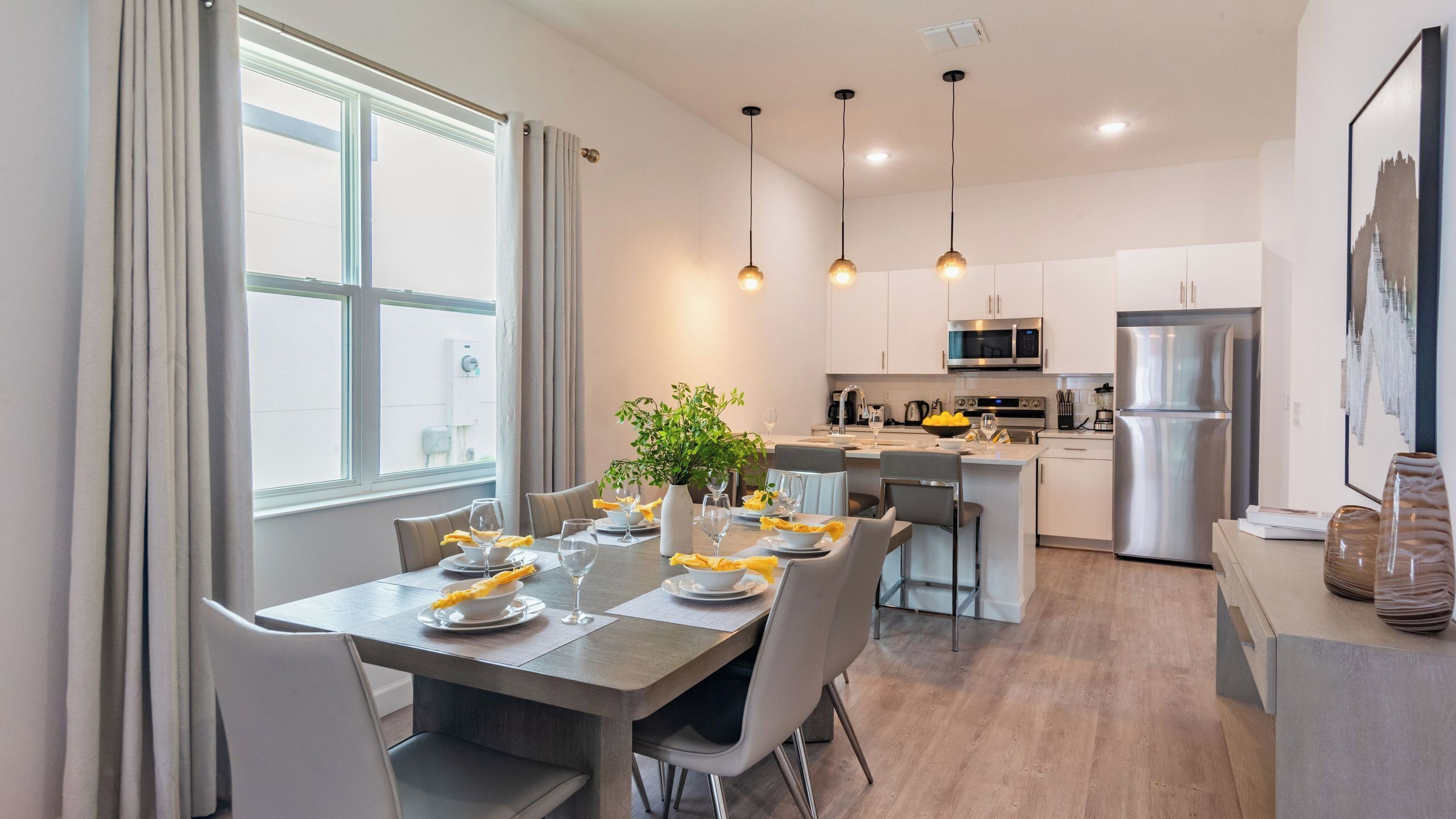 A modern kitchen with a dining area, stainless steel appliances, and a large window.