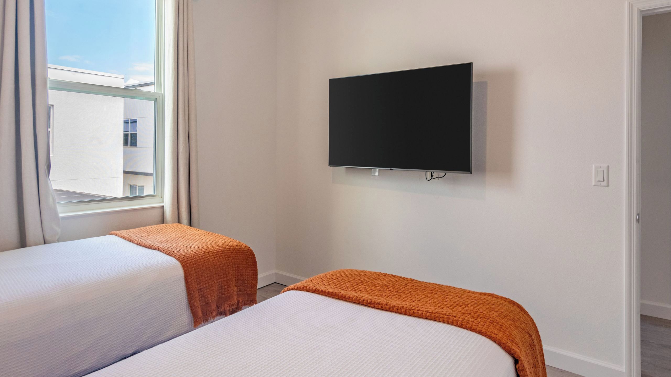 Ett hotellrum med två sängar, en platt-TV och ett fönster med gardiner.