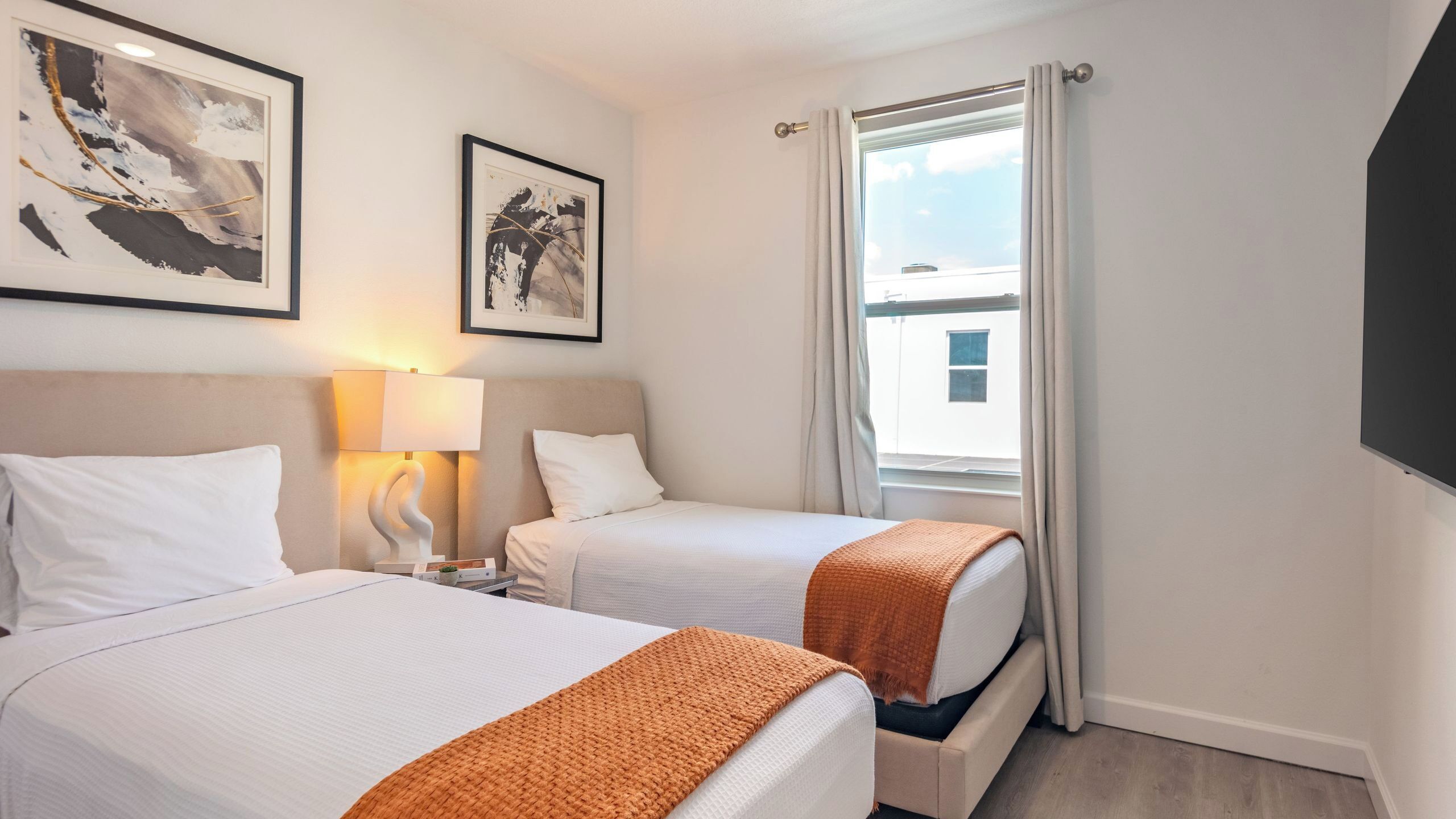 A hotel room with two beds, a nightstand with a lamp, and a window with curtains.