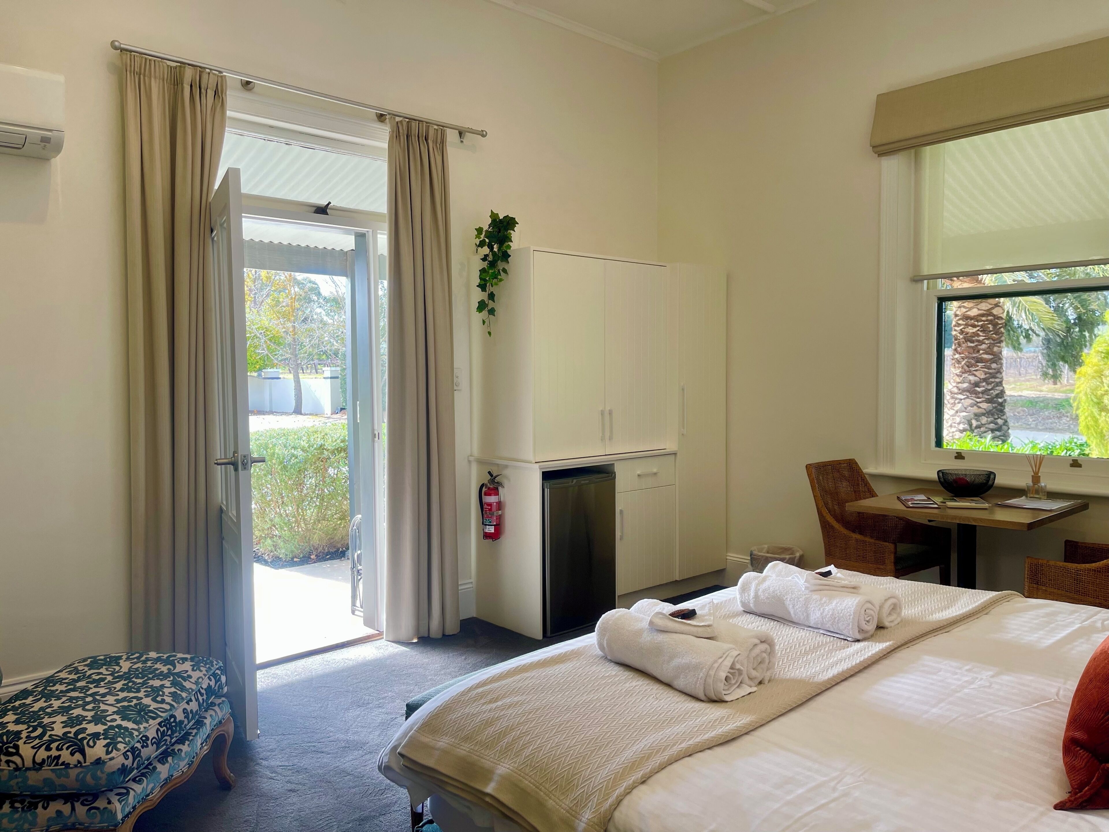 Habitación de hotel con cama, escritorio con silla, armario y ventana con vistas a la vegetación.