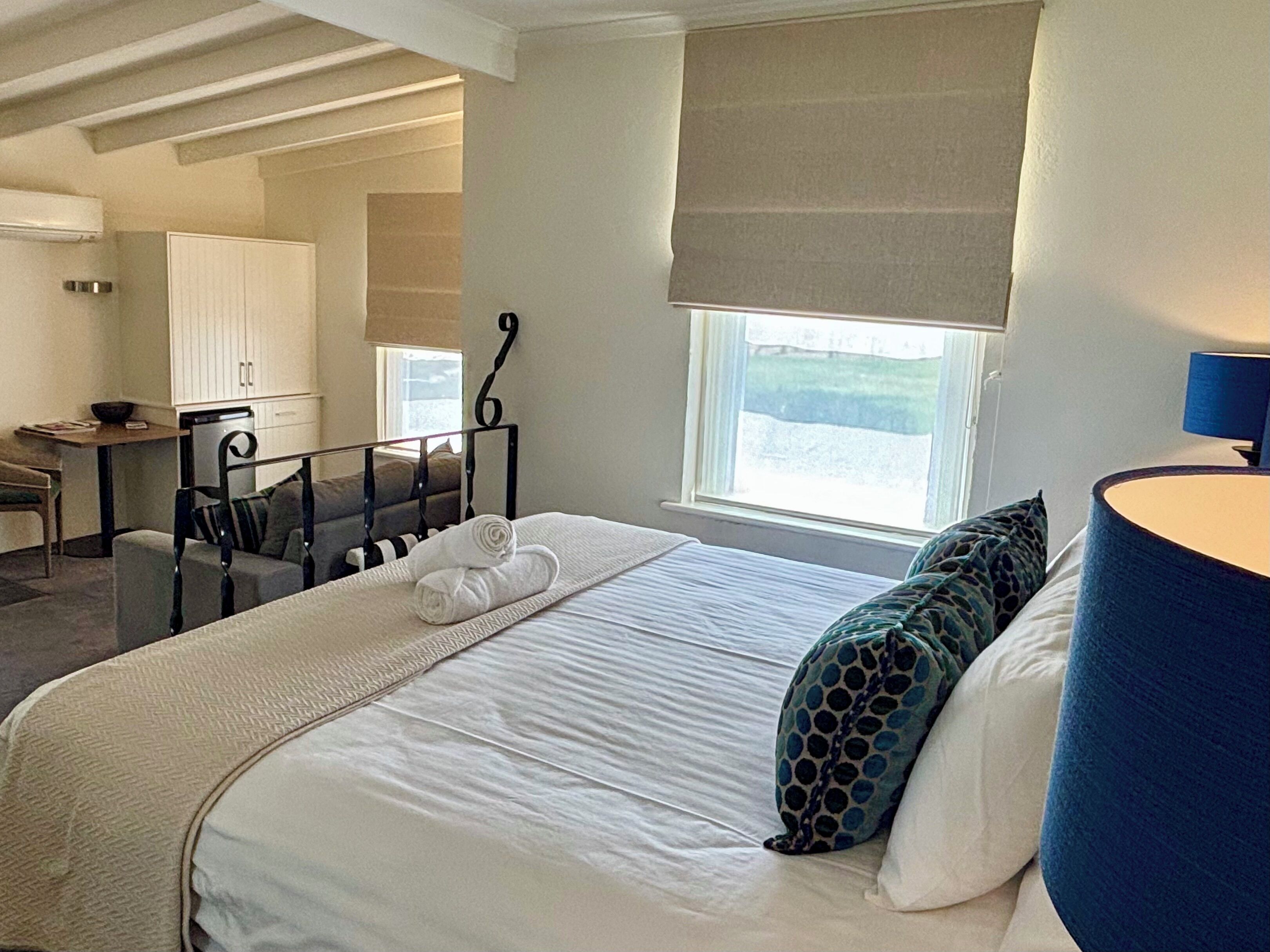 Habitación de hotel con cama, escritorio, silla, ventana con vistas y una lámpara.