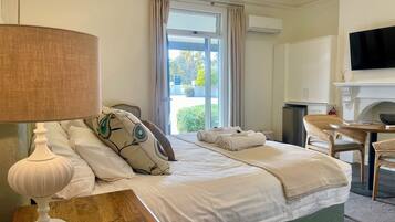 A hotel room with a bed, a wooden nightstand with a lamp, a television, a fireplace, and a window with curtains.