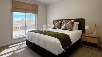Quarto com cama grande, janela com vista, mesa de cabeceira com luminária e criado-mudo.