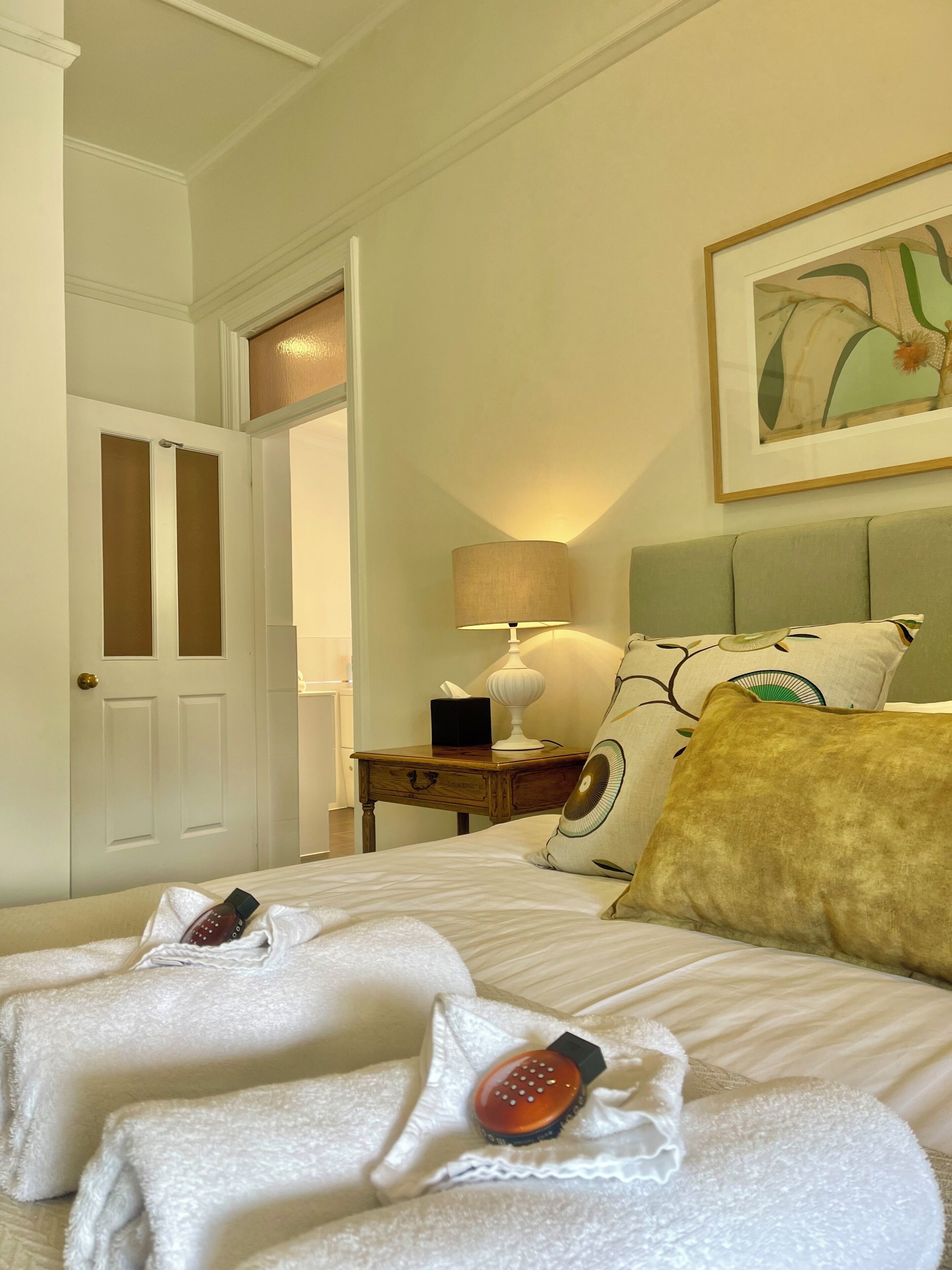 Een hotelkamer met een bed, nachtkastje, lamp en een schilderij aan de muur.