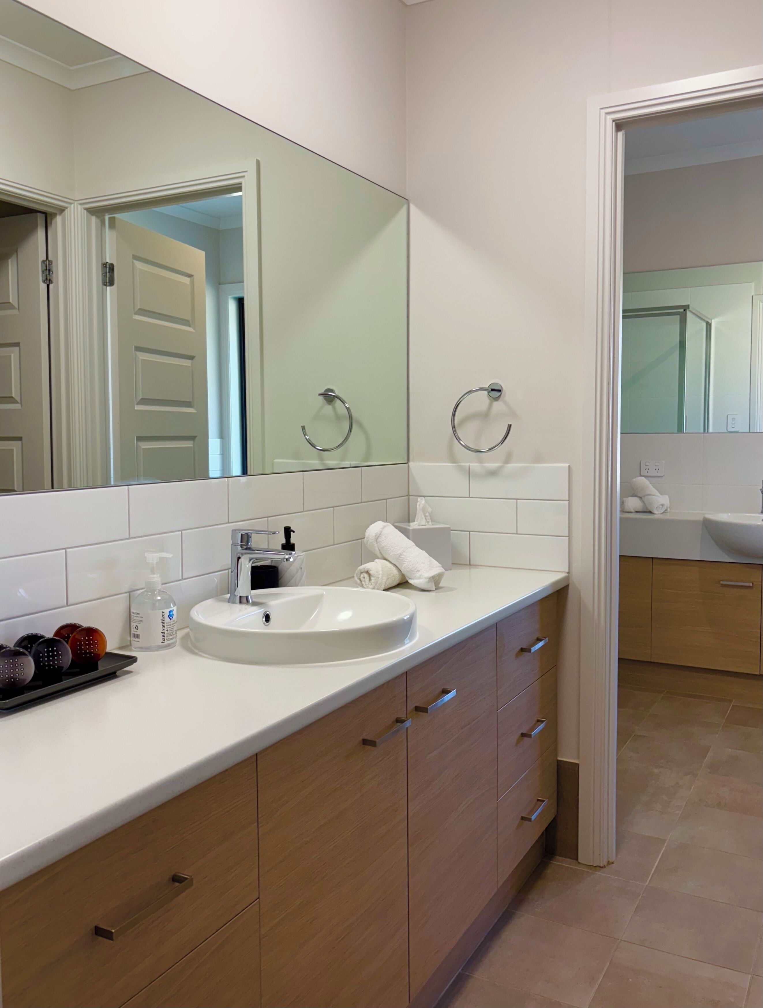 A modern bathroom with a white sink, wooden cabinets, and a large mirror.