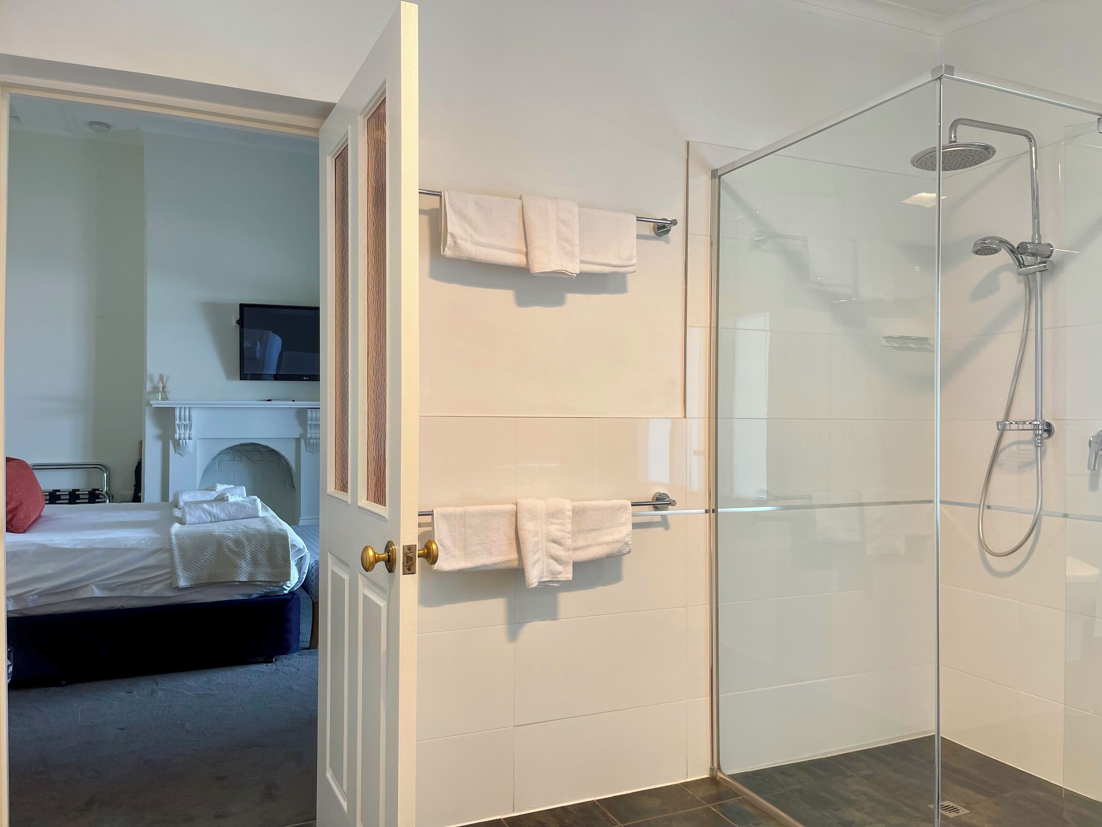 A hotel room with a bed, a fireplace, a television, and a glass-enclosed shower area.