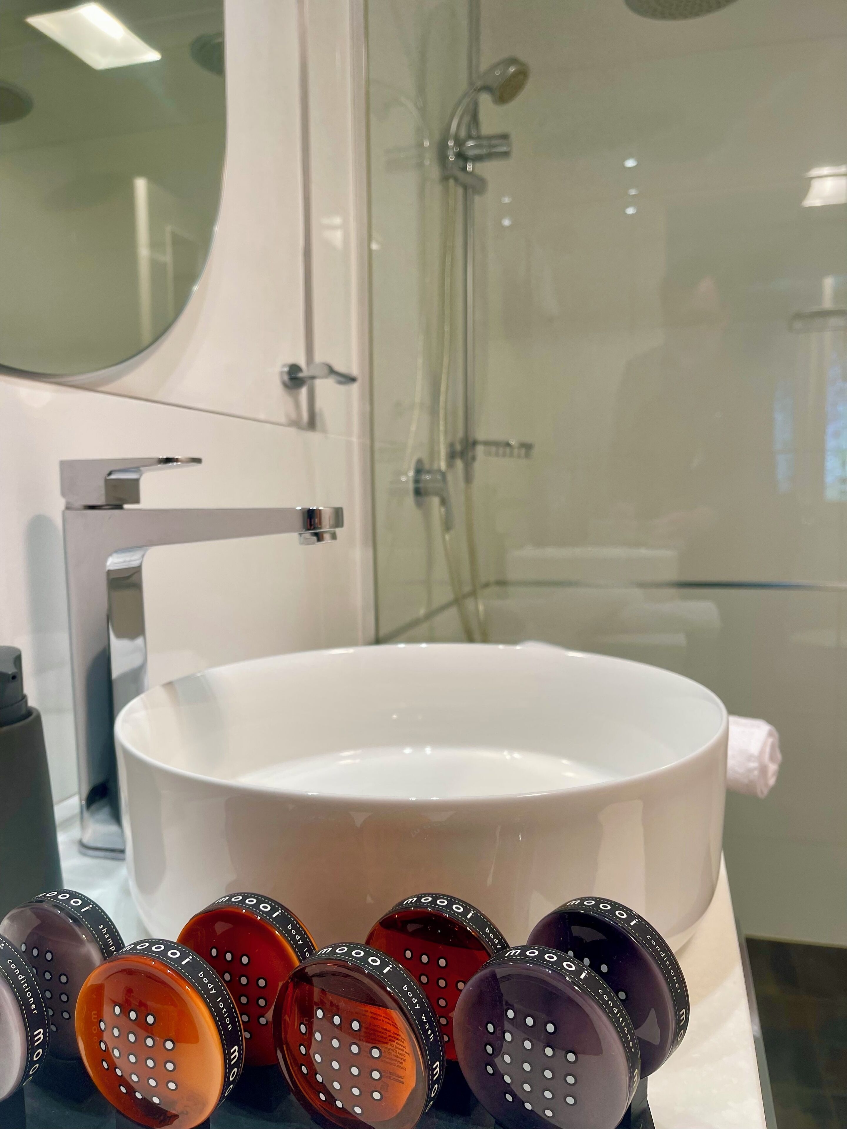 A bathroom with a large white basin, a glass shower enclosure, and a mirror.