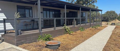 Een modern gebouw met een overdekt terras, een grindpad en een kleine tuin met planten en een bloempot.