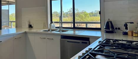 A modern kitchen with white cabinets, a gas stove, a sink, and a window overlooking a vineyard.