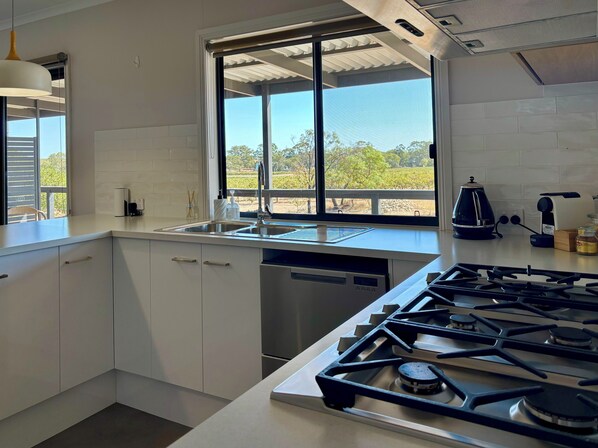 A modern kitchen with white cabinets, a gas stove, a sink, and a window overlooking a vineyard. - Pirathon Country Estate (Tanunda)