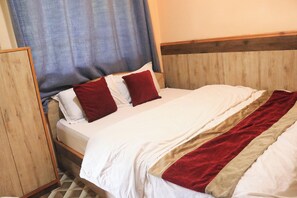 A neatly made bed with white and red bedding, a wooden headboard, and a wooden wardrobe to the left. - Dream House Resort (Panchkhal)