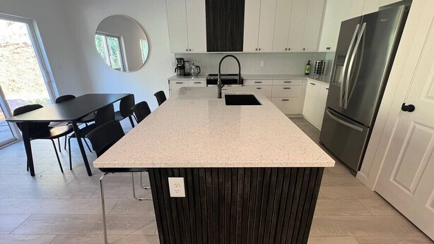 Cozinha moderna com ilha central, armários brancos e eletrodomésticos de aço inoxidável.