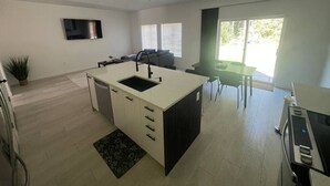 Uma cozinha moderna com ilha central, sala de jantar com mesa e cadeiras, e televisão de tela plana na parede.