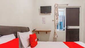 Un dormitori amb llit, televisió, una porta i finestra amb cortina.