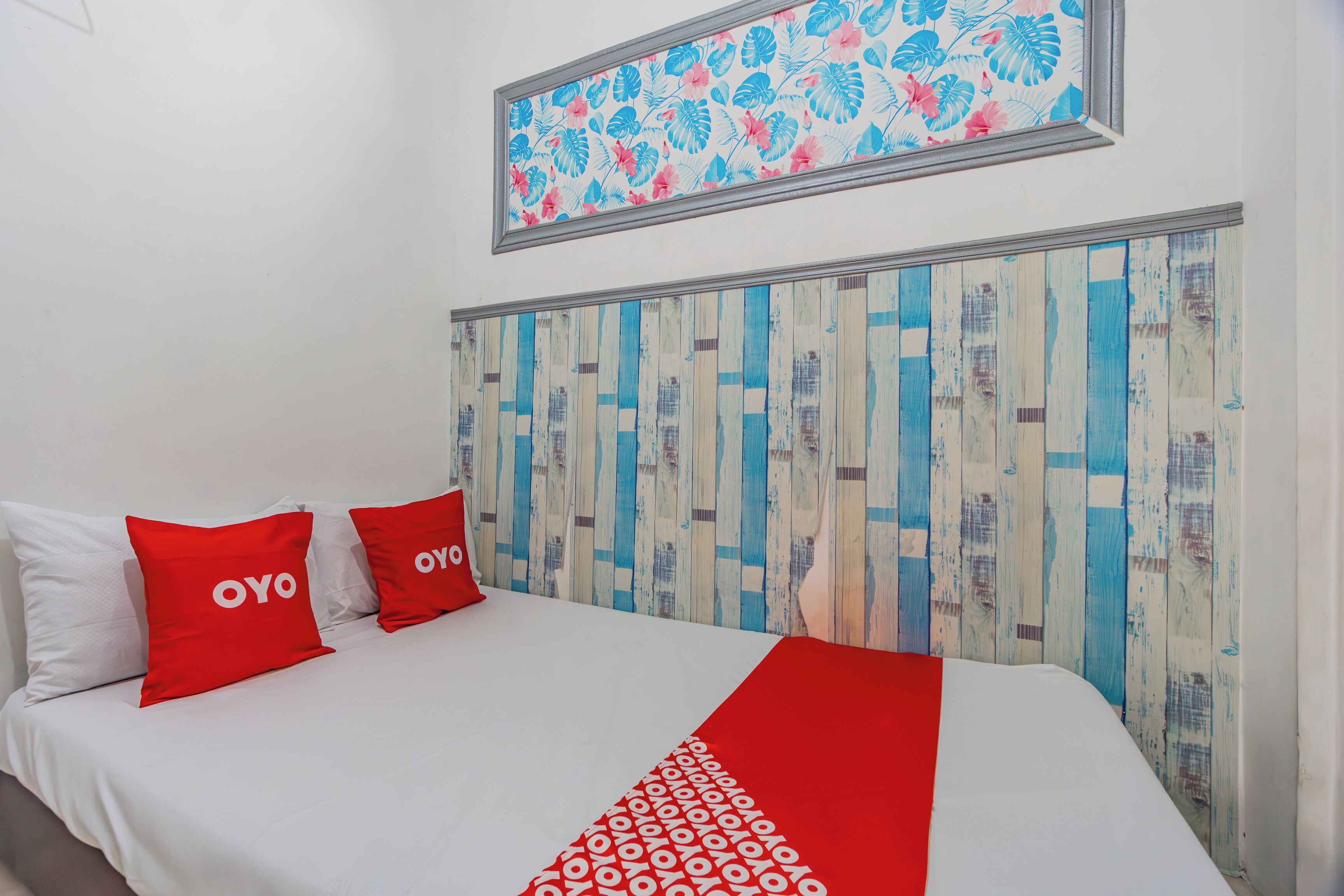 A bed with white and red bedding, two red pillows with "OYO" text, and a wooden headboard with a blue and white pattern.