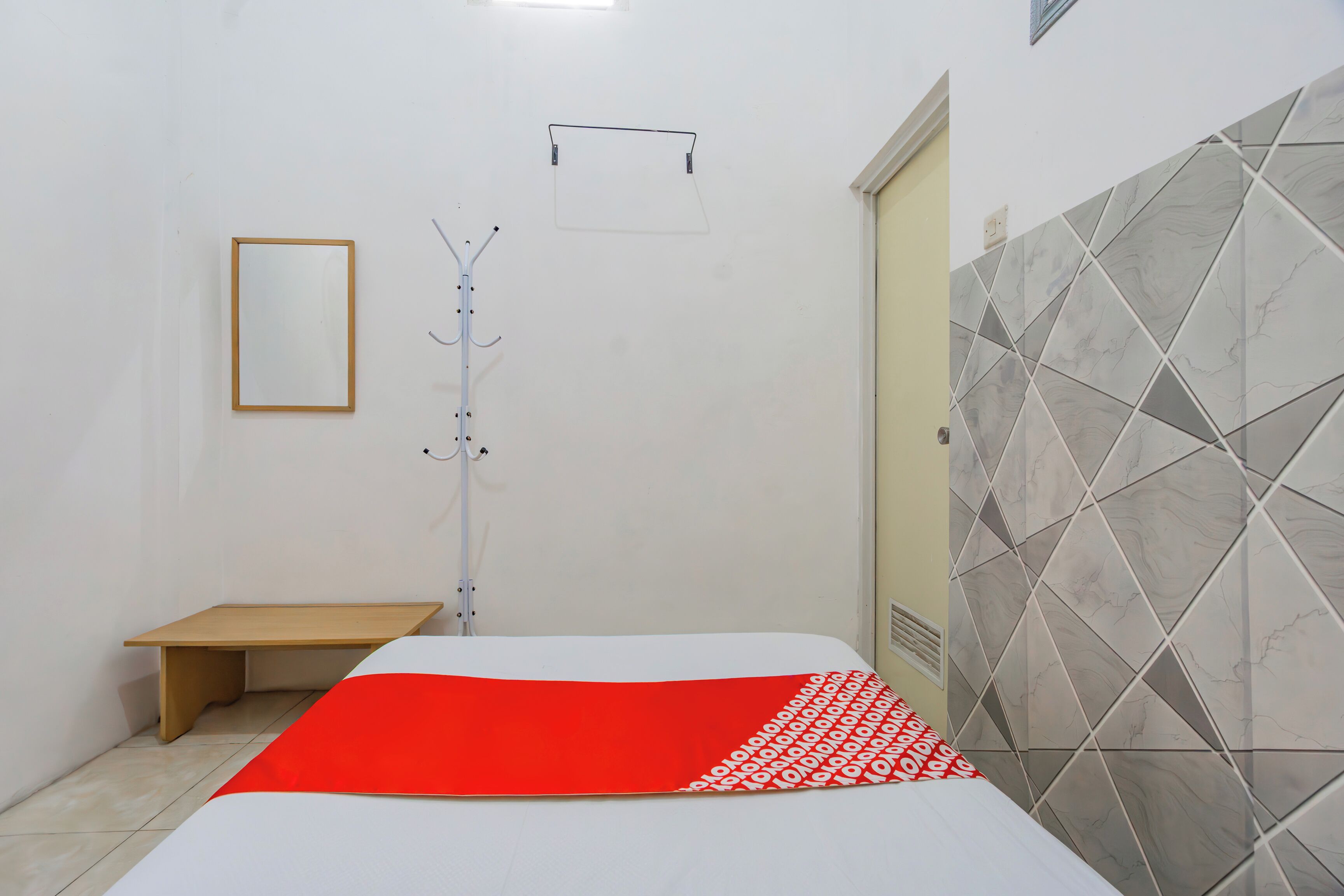 A bedroom with a bed, a wooden bench, a mirror, and a shower area with tiled walls.