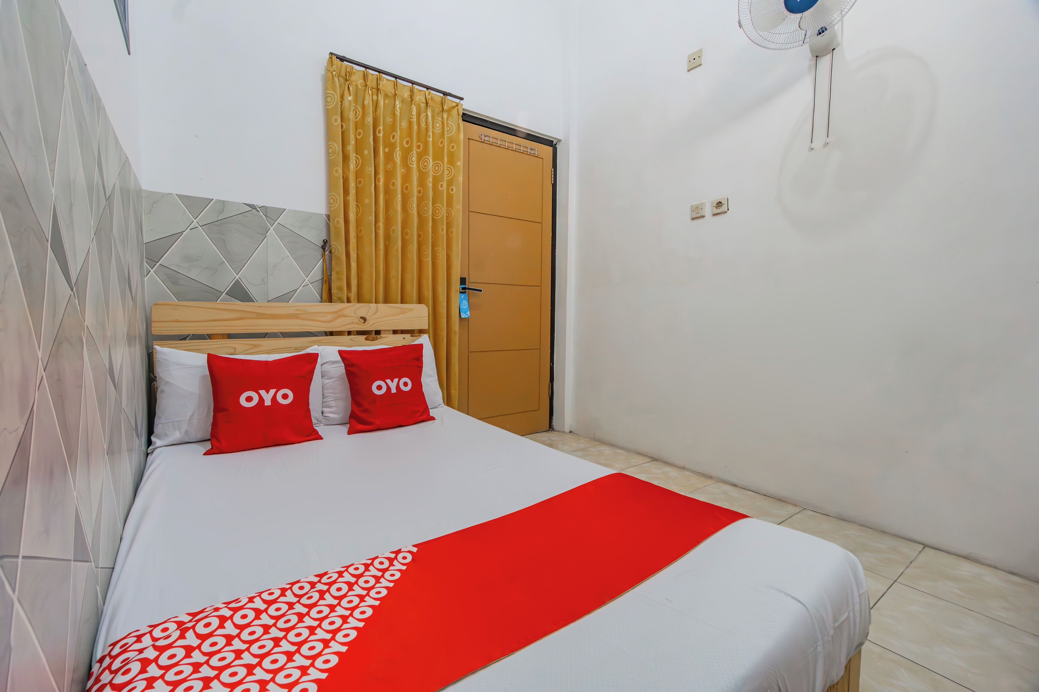 A hotel room with a bed, a wooden headboard, a red and white bedspread, and a yellow curtain.