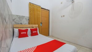 Ένα δωμάτιο ξενοδοχείου με ένα κρεβάτι, ένα ξύλινο προσκέφαλο, ένα κόκκινο και λευκό σεντόνι και μια κίτρινη κουρτίνα.