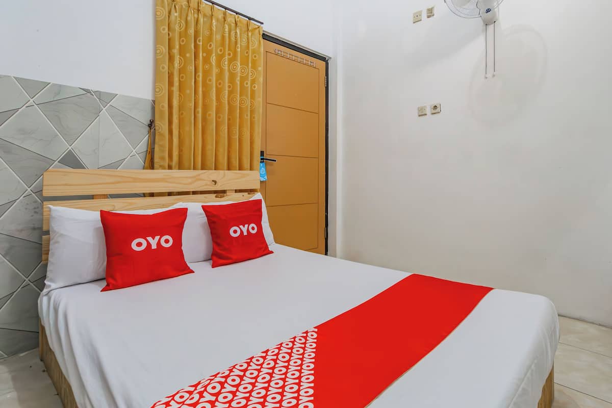 A neatly made bed with a white and red bedspread, two red pillows with the word "OYO" on them, a wooden headboard, and a yellow curtain.