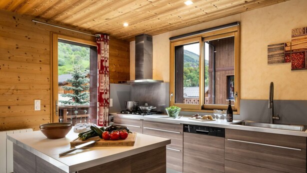 A modern kitchen with wooden cabinetry, a central island, and a view of greenery outside.