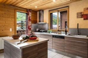 A modern kitchen with wooden cabinetry, a central island, and a view of greenery outside.