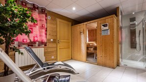 A sauna room with wooden walls, a glass door leading to a shower area, and a magazine on a chair.
