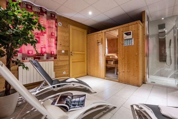 A sauna room with wooden walls, a glass door leading to a shower area, and a magazine on a chair.