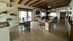A spacious kitchen with wooden beams, a dining area with green chairs, and a view of the outdoors.