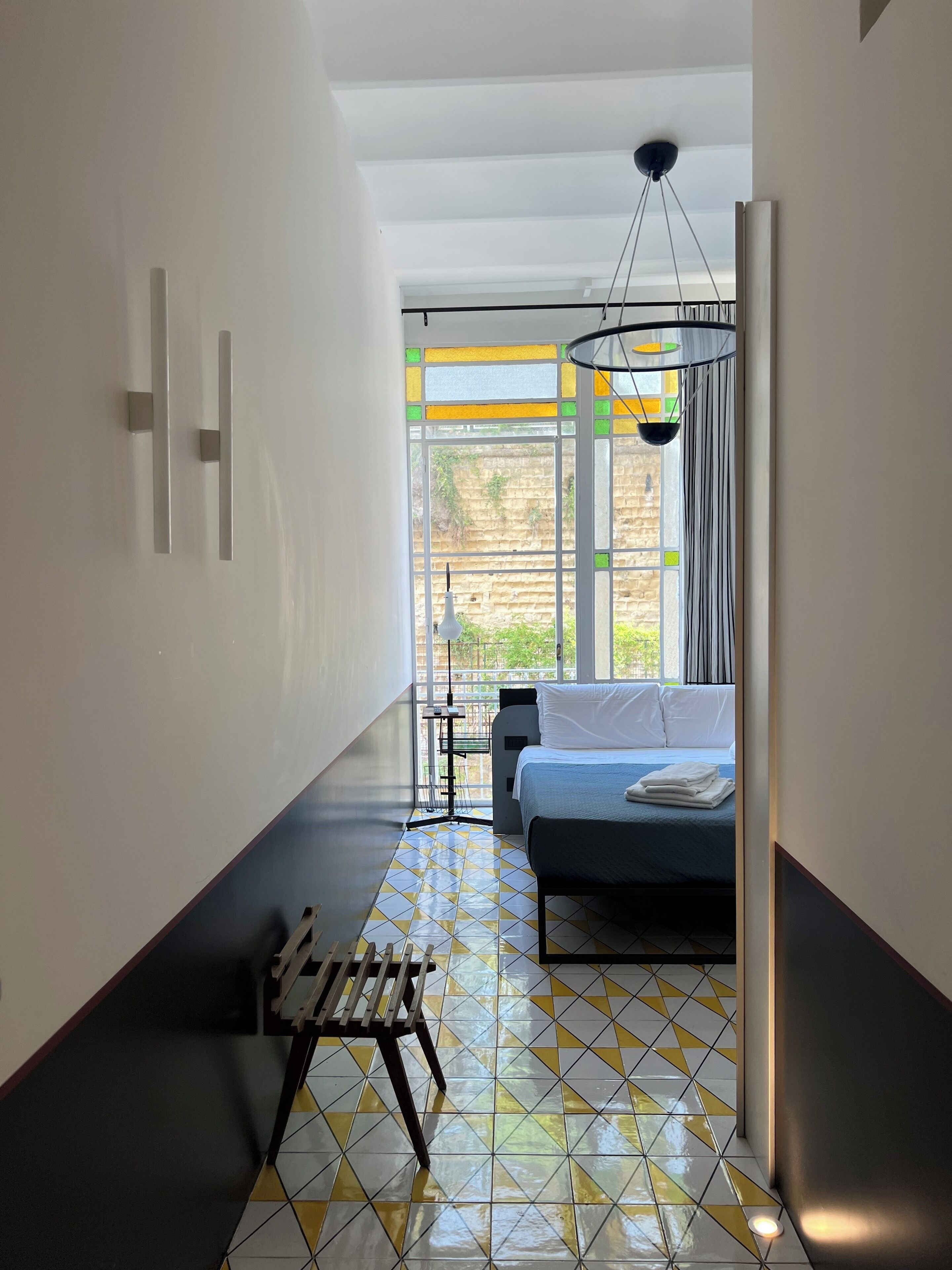 A modern hotel room with a bed, a bench, and a view of the outdoors.