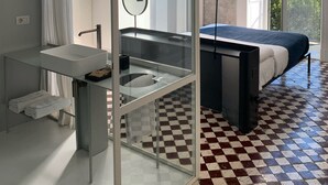Ein modernes Schlafzimmer mit einer Glastrennwand, einem Bett, einem Schreibtisch und Meerblick.
