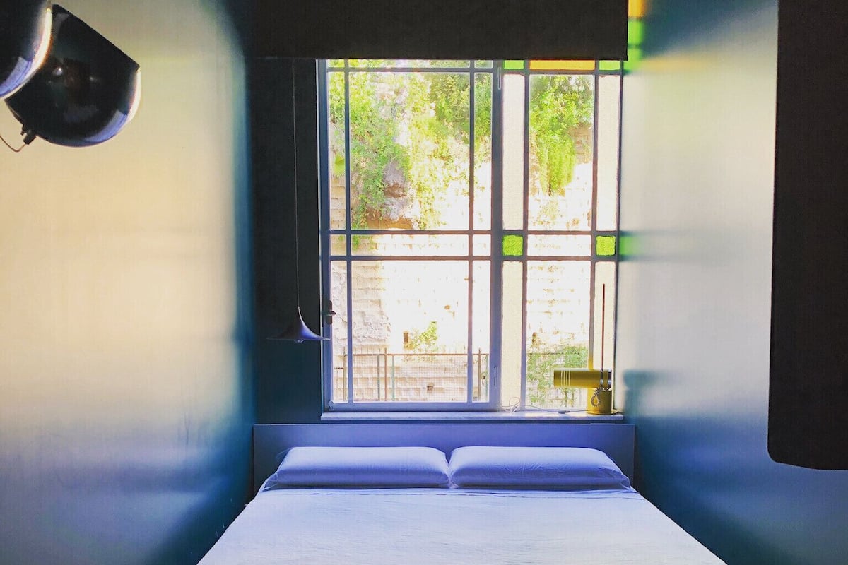 A room with a bed, a window, and a wall-mounted lamp.