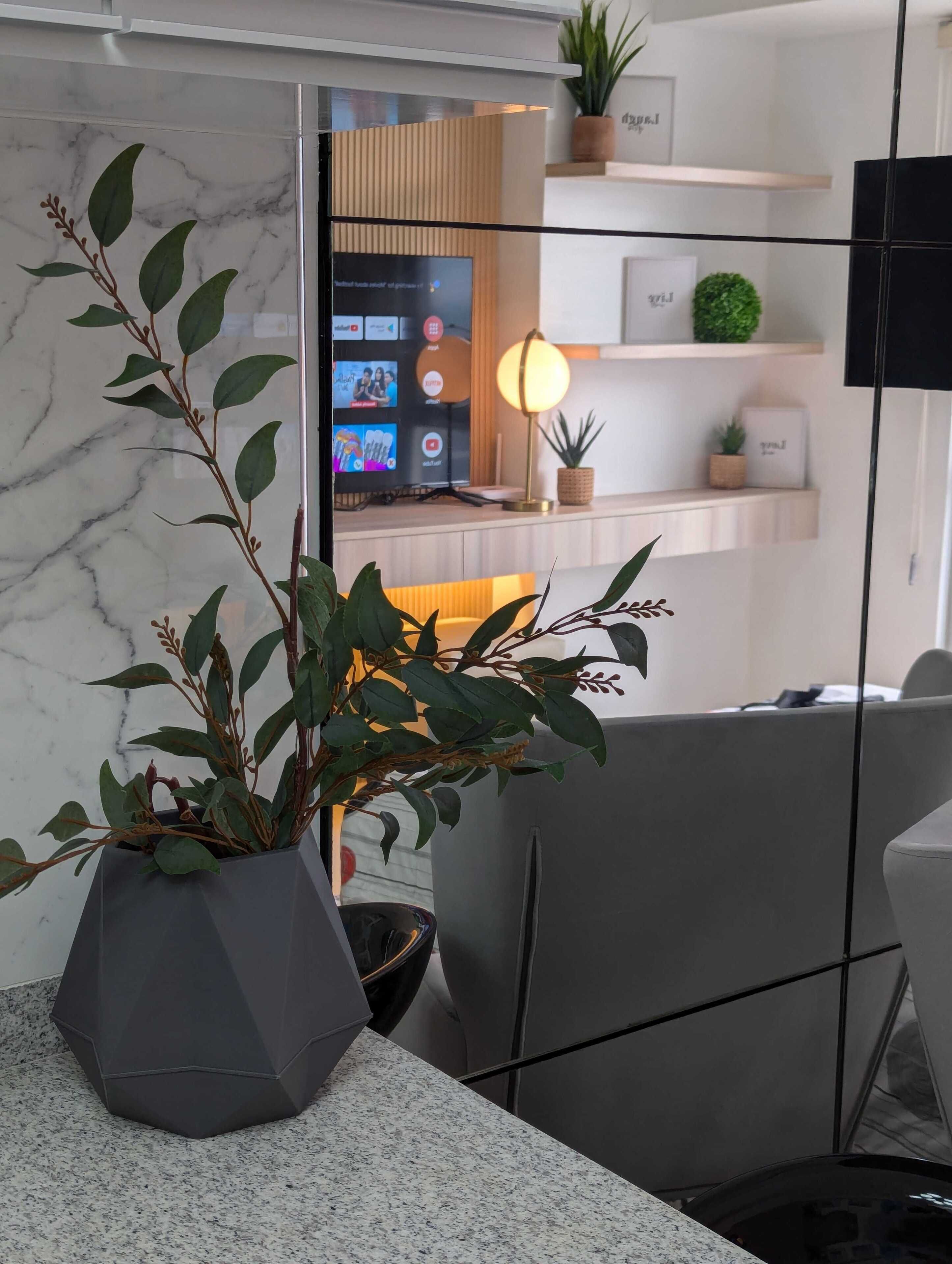 A modern office space with a marble wall, a large potted plant, a desk with a computer, and a shelf with decorative items.
