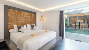 A modern bedroom with a large bed, a wooden headboard, a hanging light fixture, and a view of an outdoor pool area. - Villa Alami by Villa Finder (Seminyak)