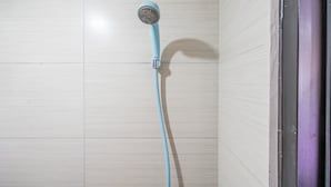 Eine Dusche mit blauem Schlauch in einem Badezimmer mit hell geflieste Wänden.