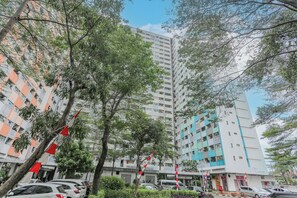 A multi-story residential building with balconies, surrounded by trees and parked cars.