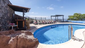 A pool area with lounge chairs, a stone wall, and a pergola.