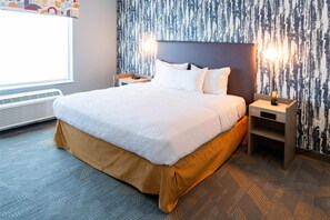 A neatly made bed with white linens, a brown skirt, and two bedside tables with lamps. - Home2 Suites BY Hilton Effingham (Effingham)