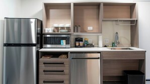 Une cuisine compacte équipée d’un réfrigérateur en acier inoxydable, d’un four à micro-ondes, d’un lave-vaisselle et de meubles de rangement en bois.