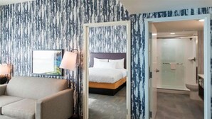 Une chambre d’hôtel avec un lit, un canapé, un tableau encadré et une salle de bain visible à travers une porte ouverte.
