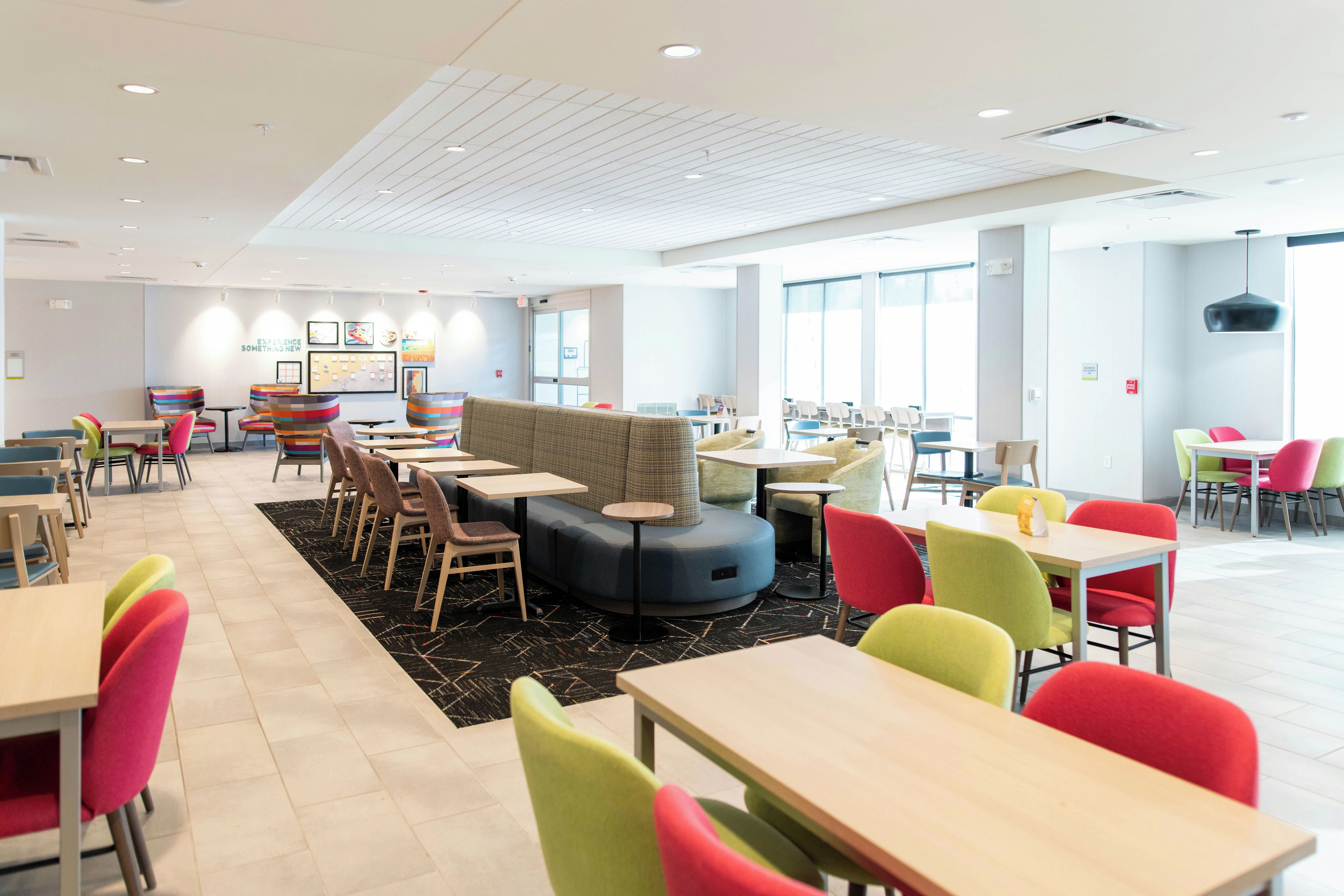 A modern hotel lobby with seating areas, tables, and a large window providing natural light.