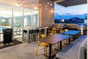 An outdoor patio with tables, chairs, a barbecue grill, and a pool.
