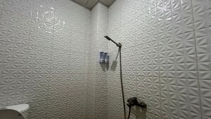 Un baño con ducha, paredes blancas con textura y un inodoro.
