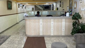 Zona de recepción con mostrador, recepcionista, una escalera al fondo y una planta en maceta.