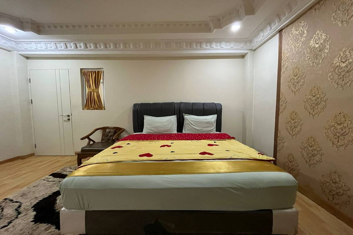 Un dormitorio con cama, una puerta, un ventanal con cortinas y papel tapiz estampado.