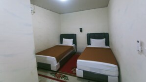Una habitación pequeña y estrecha con dos camas individuales, alfombra roja y una lámpara en el techo.