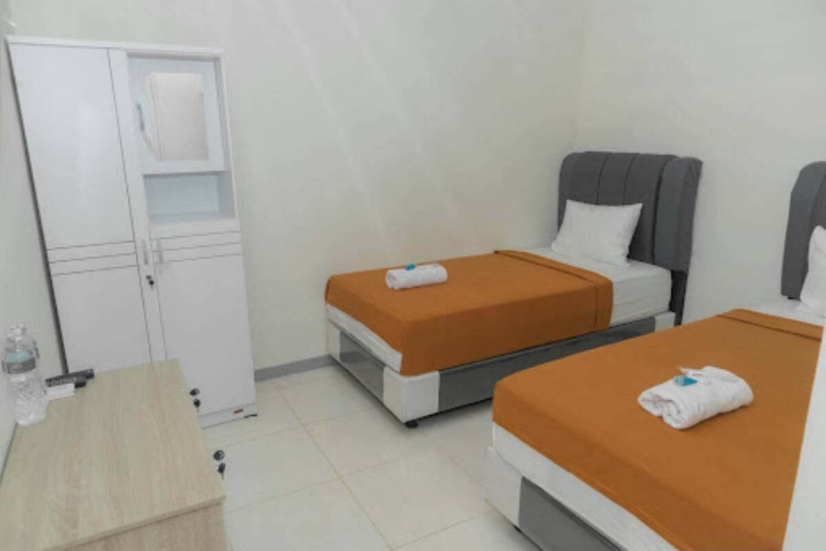 Habitación de hotel con dos camas, un armario y una mesita con una botella.