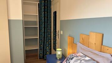 A bedroom with a bed, a nightstand, a lamp, a wardrobe, and a door with curtains.
