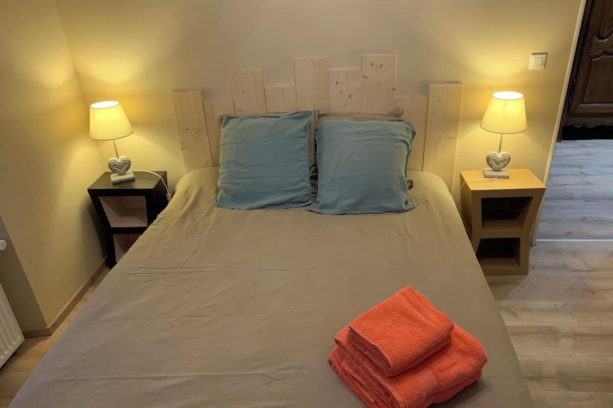 Un lit recouvert d’une couvre-lit beige, deux oreillers bleus et deux tables de chevet ornées de lampes et de décorations en forme de cœur.