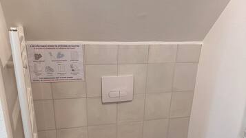 A small bathroom with a toilet, a yellow trash bin, a hand dryer, and a cabinet.